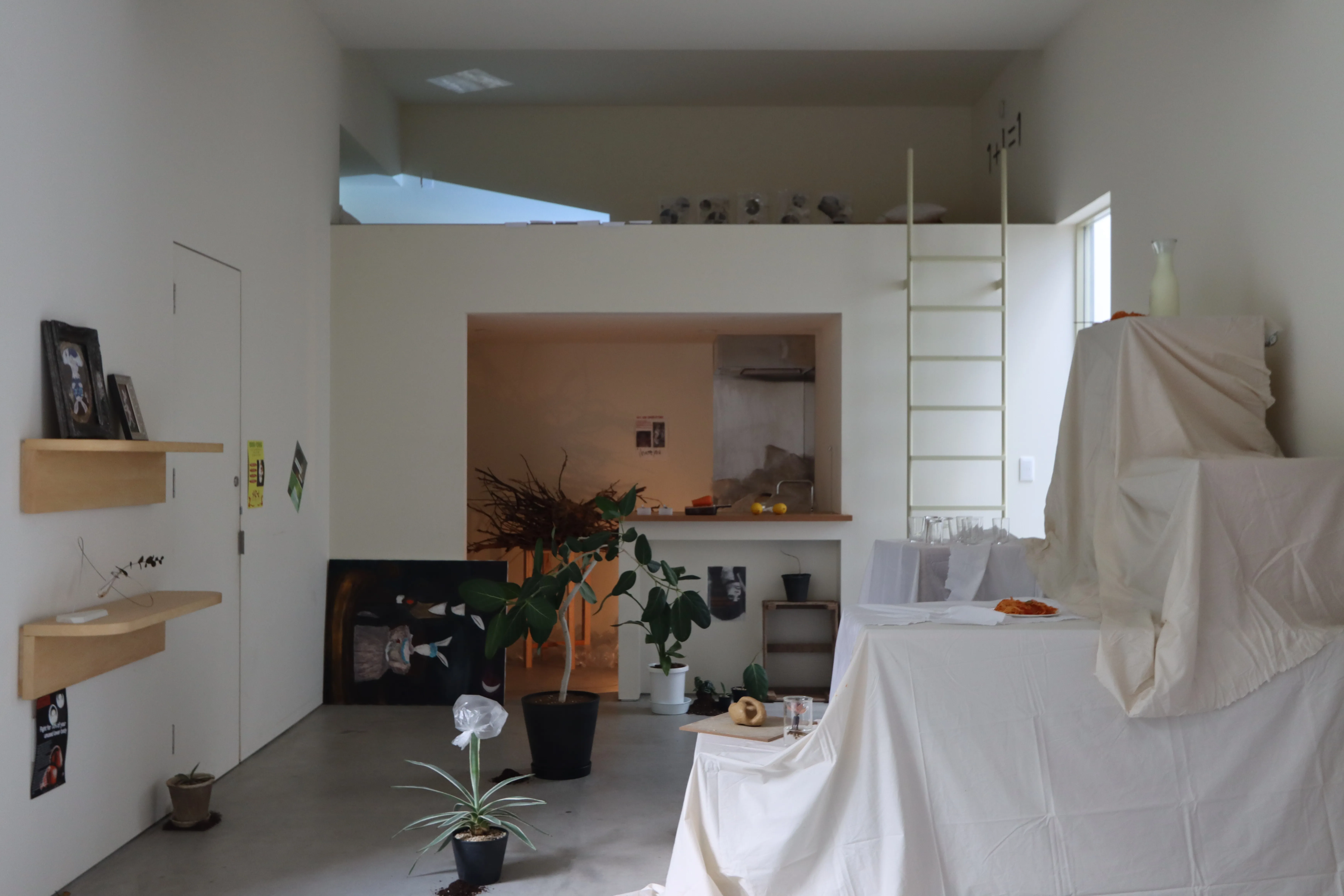 A room with a loft and kitchen, plants, and objects covered in white cloth